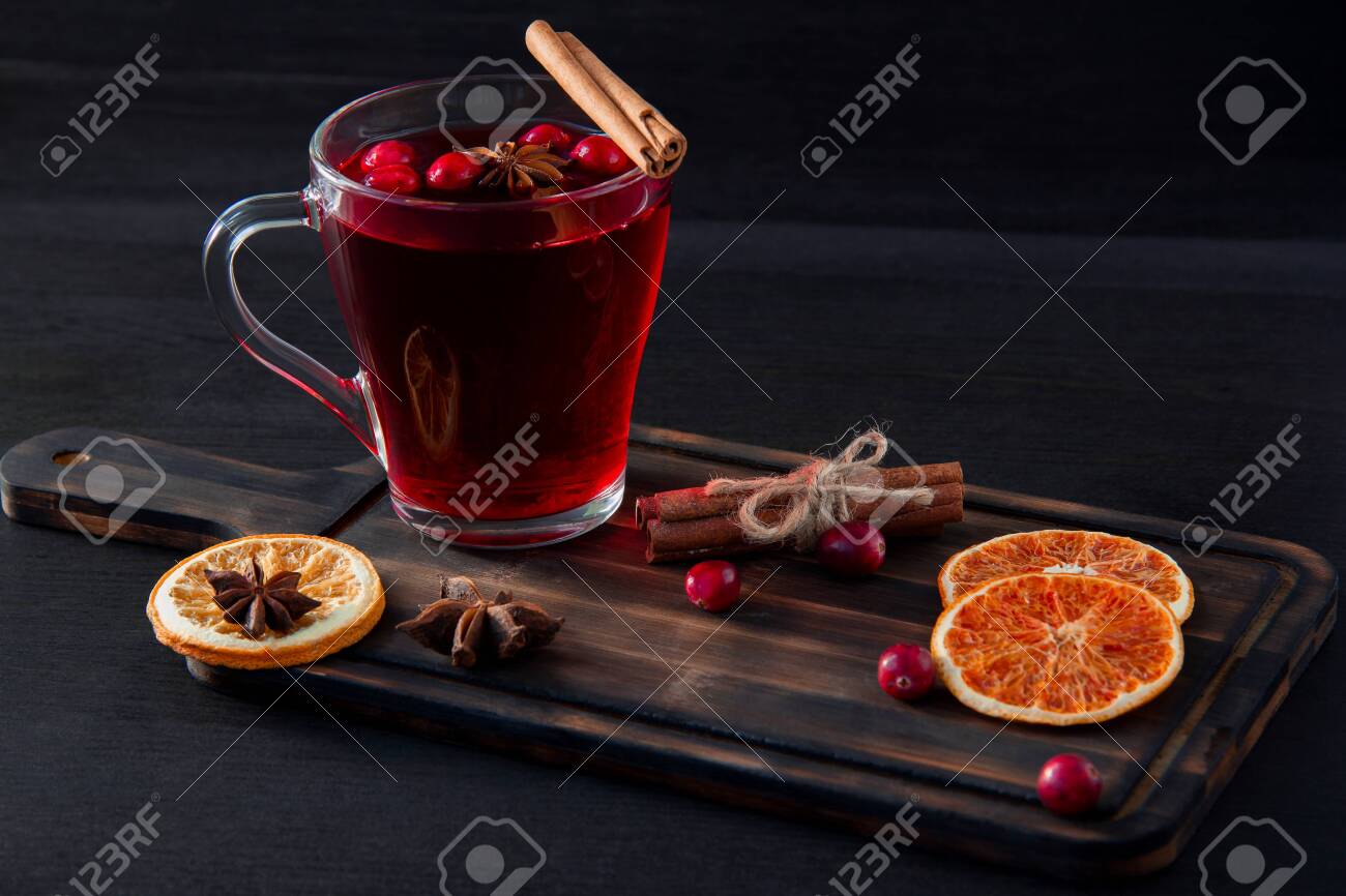 Drink from fresh cranberries in a glass on a dark wooden cutting Board. Orange slices, cinnamon and anise on a dark background. The idea of winter vitamin drinks